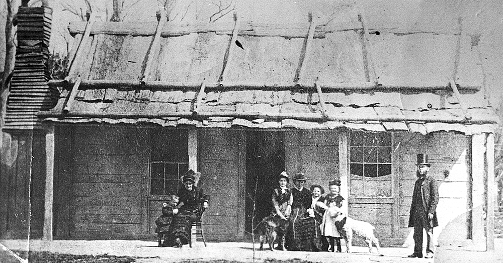 Mrs Kelly At Home Ellen Kelly’s release from prison in February 1881 is commemorated by this photo taken at the Kelly homestead. It shows from left, Alice King, Kate Kelly, Grace Kelly (with Faith, the Kelly cattle dog), Mrs Kelly, Jack King, Ellen King (feeding a pet lamb from a bottle) and the Rev. William Gould who had married Ellen Kelly and George King seven years earlier. Scarcely more than two months later, Constable Robert Graham visited here with Father Thomas Egan of Wangaratta and gained Mrs Kelly’s help in defusing the ongoing Kelly rebellion. Image: Max Brown
