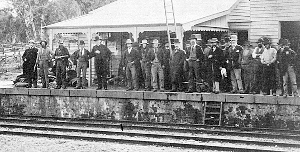 Spectators and plainclothed police pose on the railway platform in the late stages of the siege. Fifth from the left is Father Gibney. Note the group at right with their backs to the camera as they crowd around the door of the office where Ned Kelly lay. Imagine: La Trobe Collection, State Library of Victoria